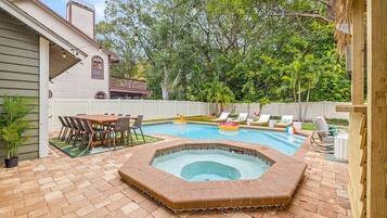 Un patio trasero con piscina, jacuzzi y un comedor con sillas y mesa.
