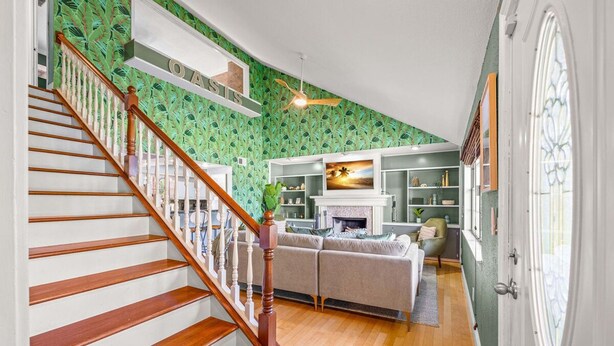 Un escalier avec des marches en bois et une rampe blanche menant à un espace de vie comprenant une cheminée, un canapé et un téléviseur.