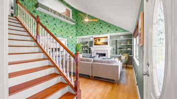 A staircase with wooden steps and a white railing leading to a living area with a fireplace, a sofa, and a television.