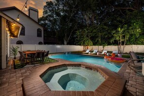 Un cortile con piscina, vasca idromassaggio e zona pranzo con mobili da esterno.