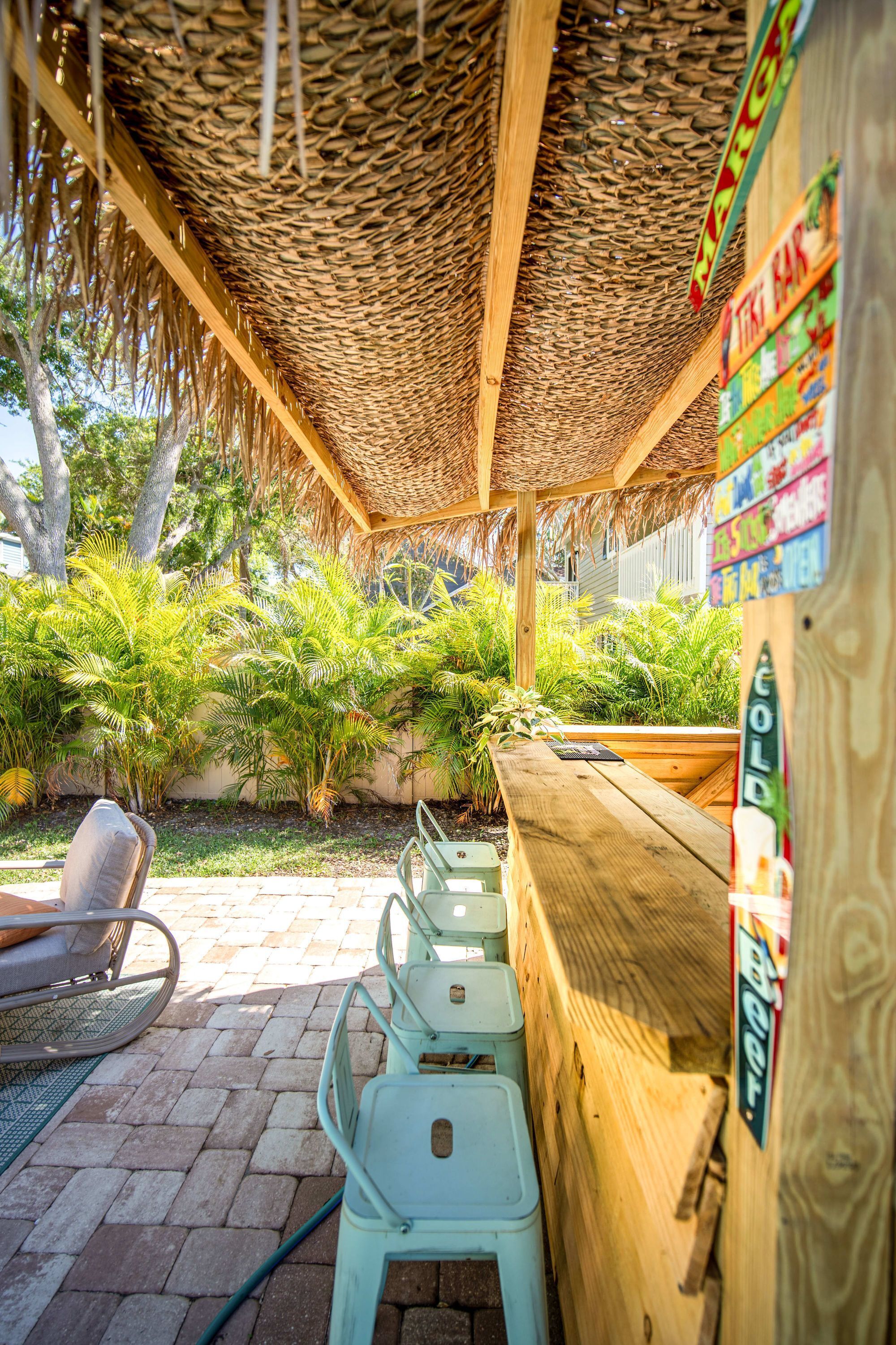 Un espacio de estar al aire libre con techo de paja, rodeado de abundante vegetación y un banco de madera.