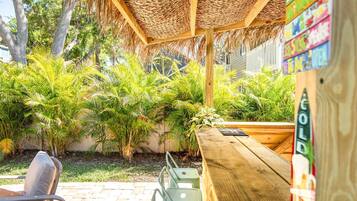 Un espacio de estar al aire libre con techo de paja, rodeado de abundante vegetación y un banco de madera.