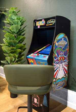 A vintage arcade machine with a colorful display, a green chair in front, and a potted plant beside it. - 1 Mile to Beach Pool Tiki Bar Mini Golf (Seminole)