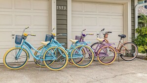 Quatre vélos sont garés devant une maison qui a deux portes de garage, chacune étant peinte d’une couleur différente.