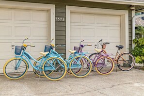 Four bicycles parked in front of a house with two garage doors, each with a different color scheme. - Tiki Bar Pool Putt Putt 1 Mile From Beach (Seminole)