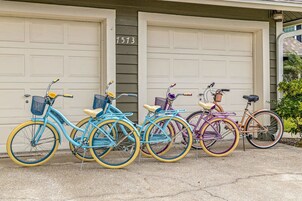 Cuatro bicicletas estacionadas frente a una casa con dos puertas de garaje, cada una con un diseño de color diferente.
