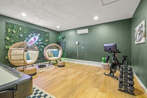 A room with two wicker chairs, a massage table, a wall-mounted air conditioner, and a bicycle with dumbbells. - 1 Mile to Beach Pool Tiki Bar Mini Golf (Seminole)