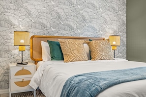 A bedroom with a bed, two bedside lamps, a nightstand, and a patterned wallpaper. - Tiki Bar Pool Putt Putt 1 Mile From Beach (Seminole)