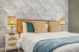 Un dormitorio con cama, dos lámparas de noche, una mesita de noche y papel tapiz estampado.