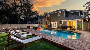A backyard with a swimming pool, lounge chairs, and a deck.