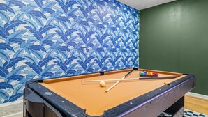 Une table de billard, avec un papier peint à motifs de feuilles bleues et un mur vert.