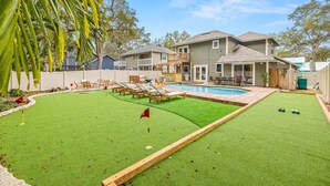 Un jardin avec une piscine, une pelouse et une terrasse en bois.