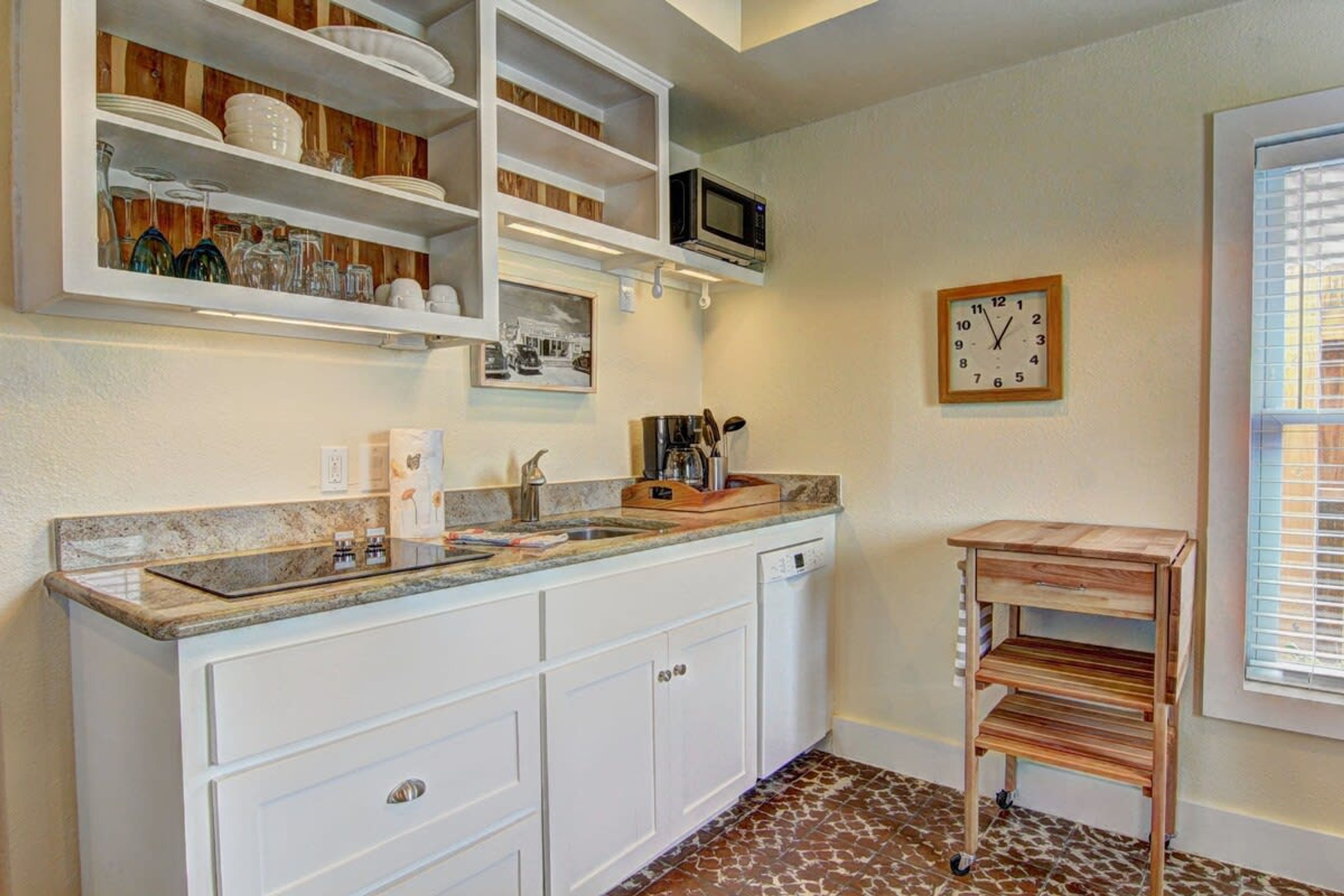 Una cocina con muebles blancos, un microondas integrado, un lavamanos y un reloj en la pared.