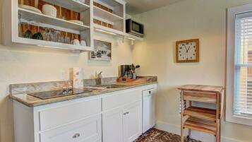 Una cocina con muebles blancos, un microondas integrado, un lavamanos y un reloj en la pared.
