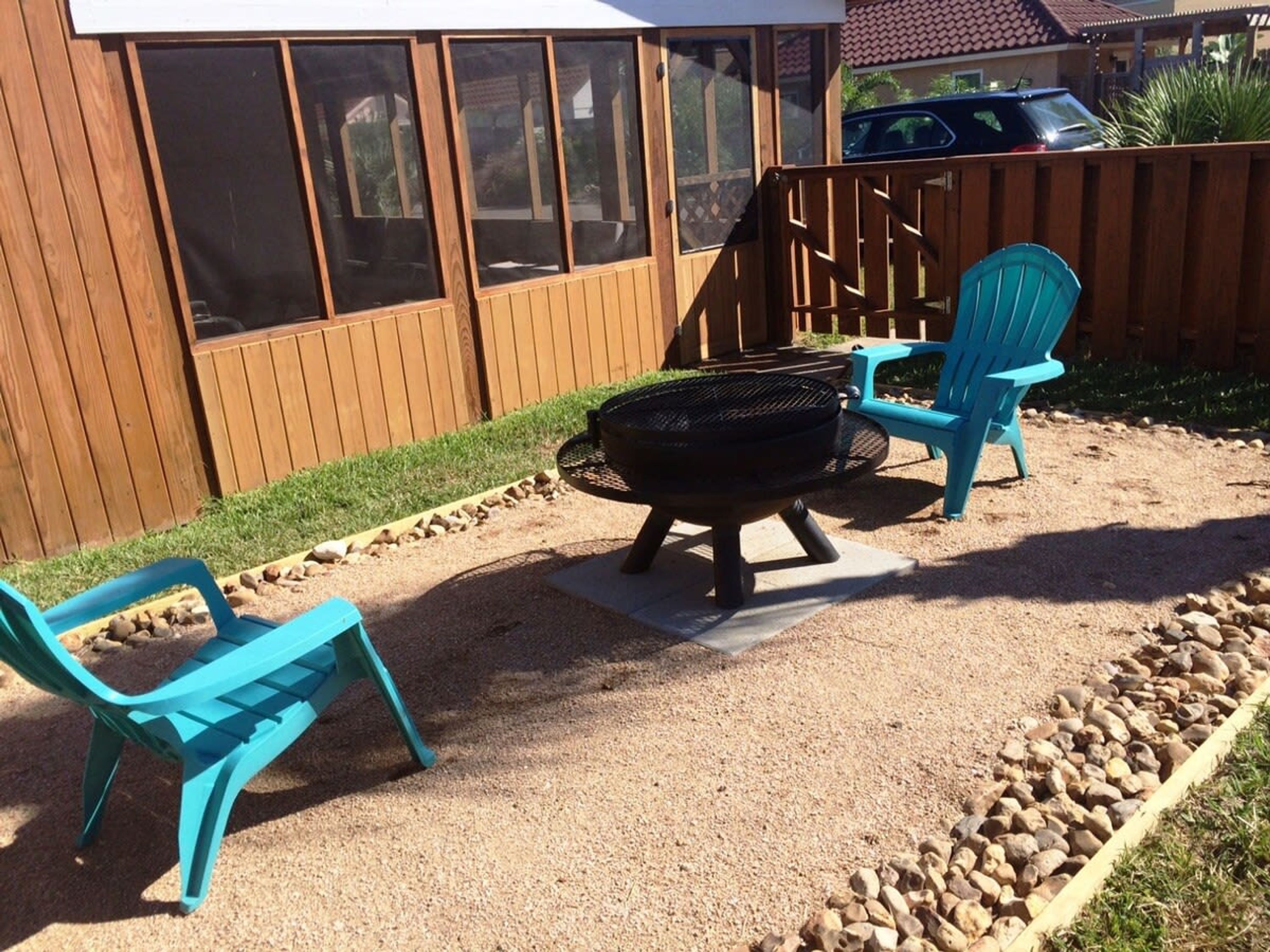 Un patio trasero con una parrilla, dos sillas turquesas y una valla de madera.