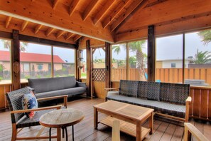 Eine offene, überdachte Terrasse mit Holzmöbeln, darunter Sofas und ein Tisch, sowie große Fenster mit Blick auf die umliegende Landschaft.