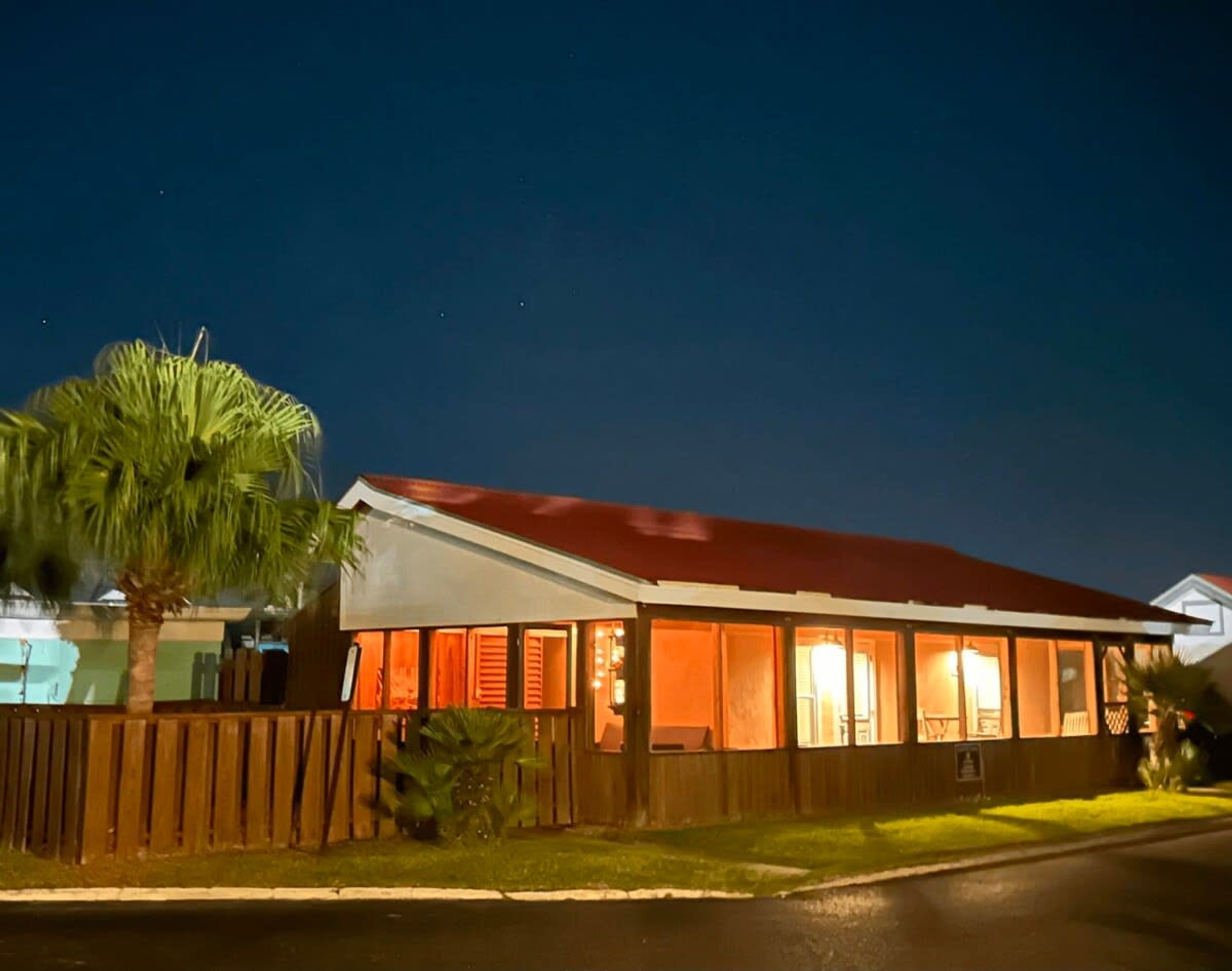 A single-story building with a red roof, a wooden fence, and a palm tree in the foreground.