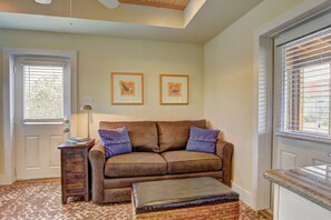 A living room with a brown sofa, two pillows, a small table, and a lamp. There are two framed pictures on the wall.