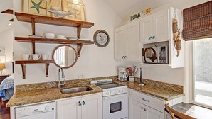 Eine Küche mit einer Granitabdeckung, einem Geschirrspüler, einem Backofen und einer Mikrowelle. Darüber befinden sich Holzregale und an der Wand hängt eine Uhr.