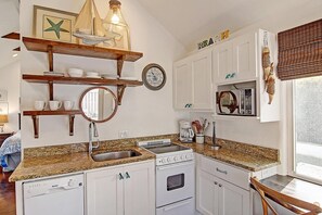 A kitchen with a granite countertop, a dishwasher, an oven, and a microwave. There are wooden shelves above the counter and a clock on the wall. - Cozy Private Cottage Pet Friendly Prime Location (Port Aransas)