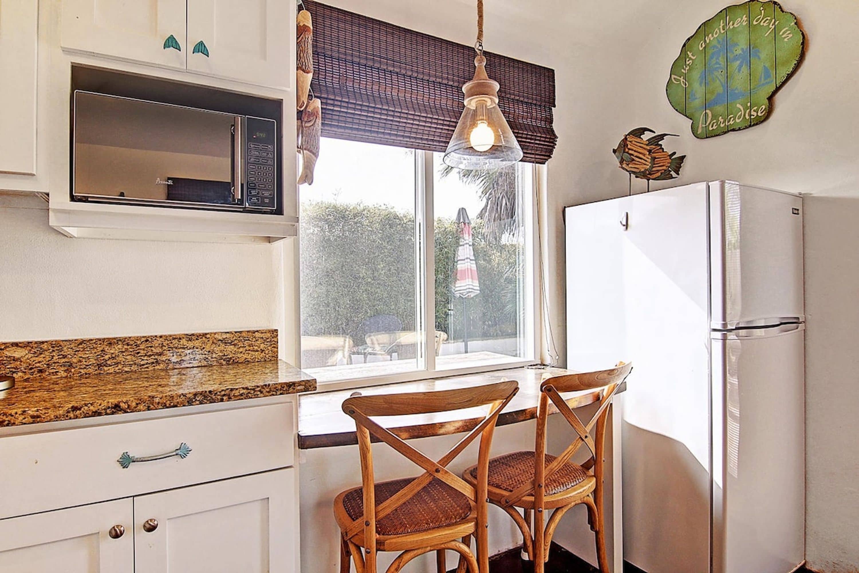 Cocina compacta con refrigerador, microondas y sillas de madera.