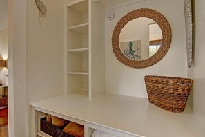 A white interior with a woven basket shelf, a round mirror, and a fireplace with a wooden log. - Cozy Private Cottage Pet Friendly Prime Location (Port Aransas)