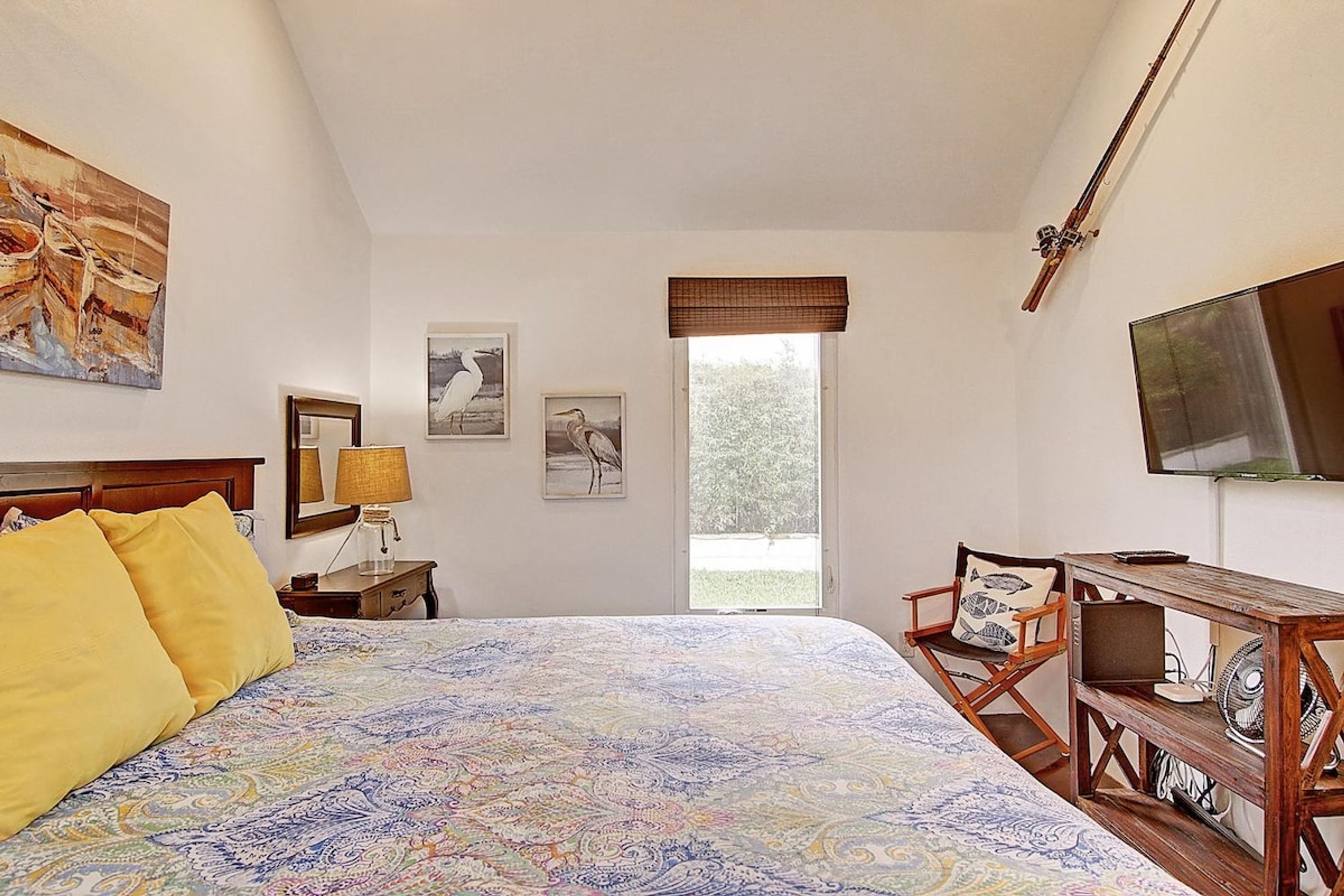 A bedroom with a large bed, a desk with a chair, a television, and artwork on the walls.