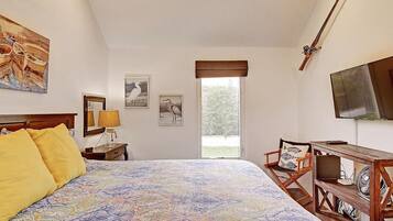 Quarto com uma cama grande, uma escrivaninha com cadeira, televisão e obras de arte nas paredes.