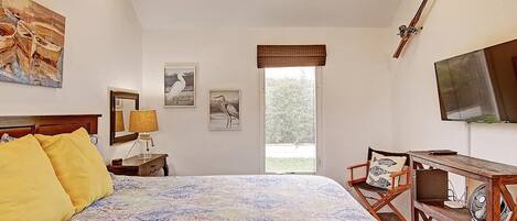 A bedroom with a large bed, a desk with a chair, a television, and artwork on the walls.