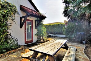 Ein Holztisch für ein Picknick in einem Garten mit einem weißen Gebäude, einer roten Tür und einem Metallzaun.