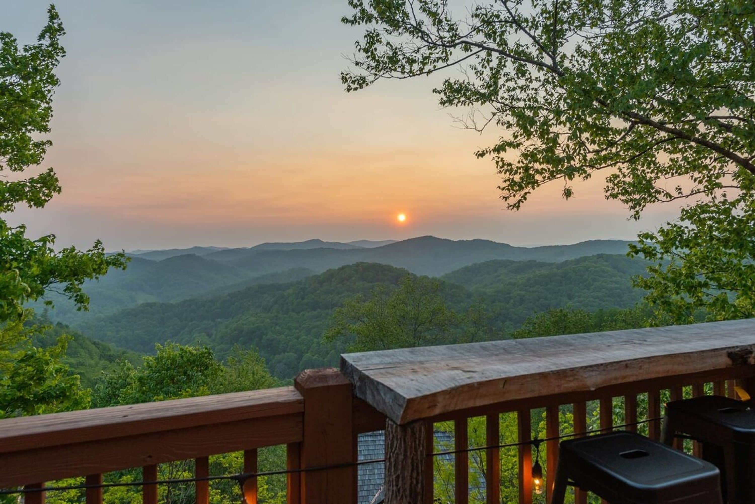 A wooden deck overlooking a mountainous landscape with a sunset.