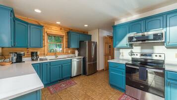 A kitchen with teal cabinets, stainless steel appliances, and a window with a view of greenery.