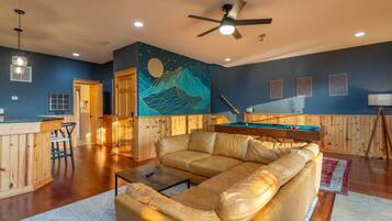 A spacious living area with a leather sofa, a pool table, and a ceiling fan.