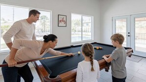 Une table de billard dans une pièce dotée de grandes fenêtres, de poutres en bois au plafond et d’un tableau encadré au mur.