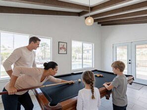 Ein Billardtisch in einem Raum mit großen Fenstern, Holzbalken an der Decke und einem gerahmten Bild an der Wand.