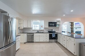 A modern kitchen with stainless steel appliances, white cabinetry, and a large window providing natural light. - 4 Br Tempe Retreat Pool Putt Putt Pool Table (Tempe)