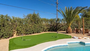 A backyard with a swimming pool, artificial grass, and a golf course setup. - Epic Desert Stay Pool Hot Tub Sports Court (Scottsdale)