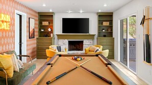 A pool table with a fireplace, a television, and a pool table setup in a living area. - Epic Desert Stay Pool Hot Tub Sports Court (Scottsdale)