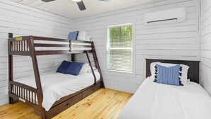 Een slaapkamer met een stapelbed, een plafondventilator, een raam met zonwering en een airconditioning.