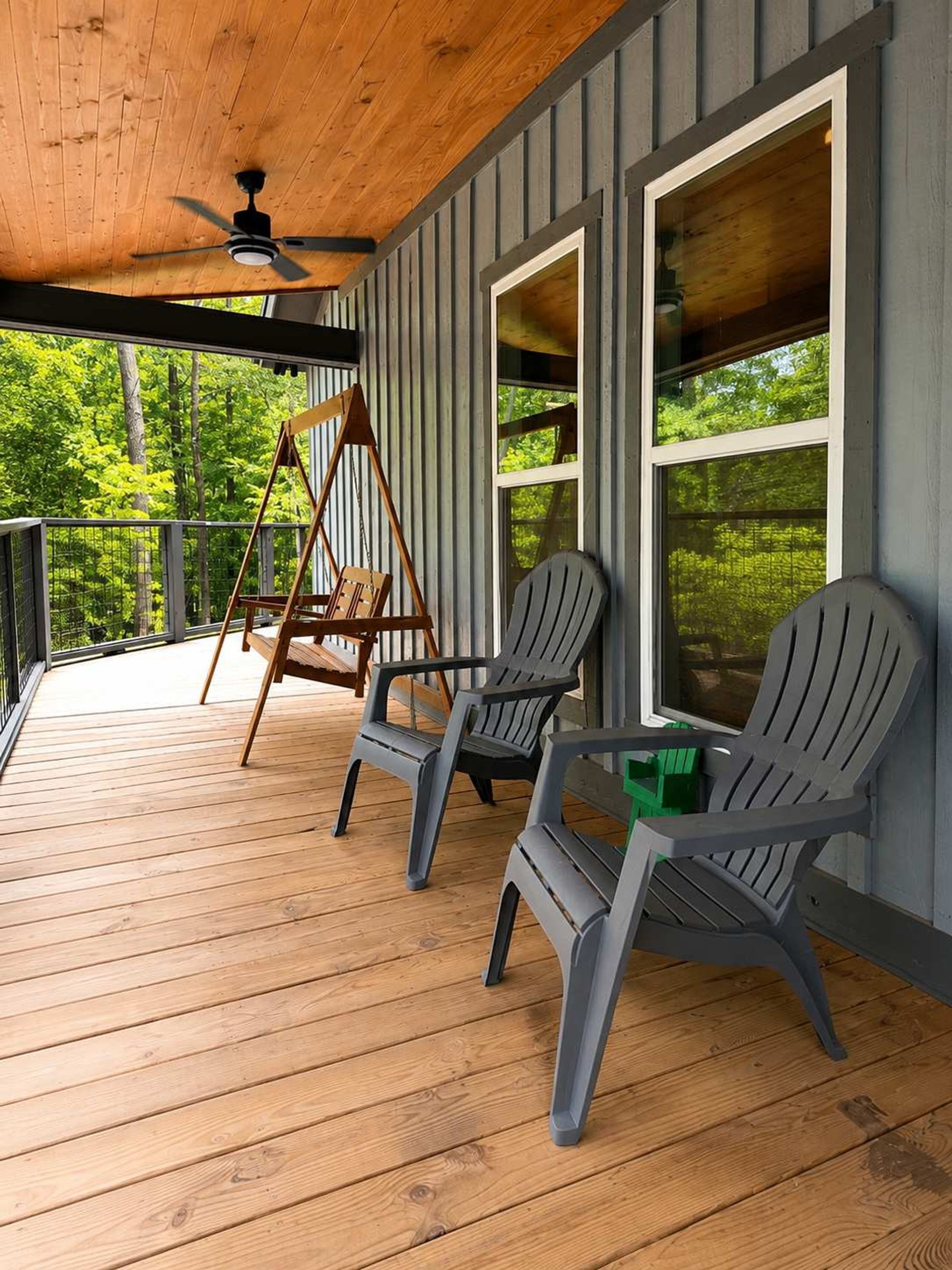 En inglasad veranda med en takfläkt, två Adirondack-stolar, en gunga och utsikt över en skog.
