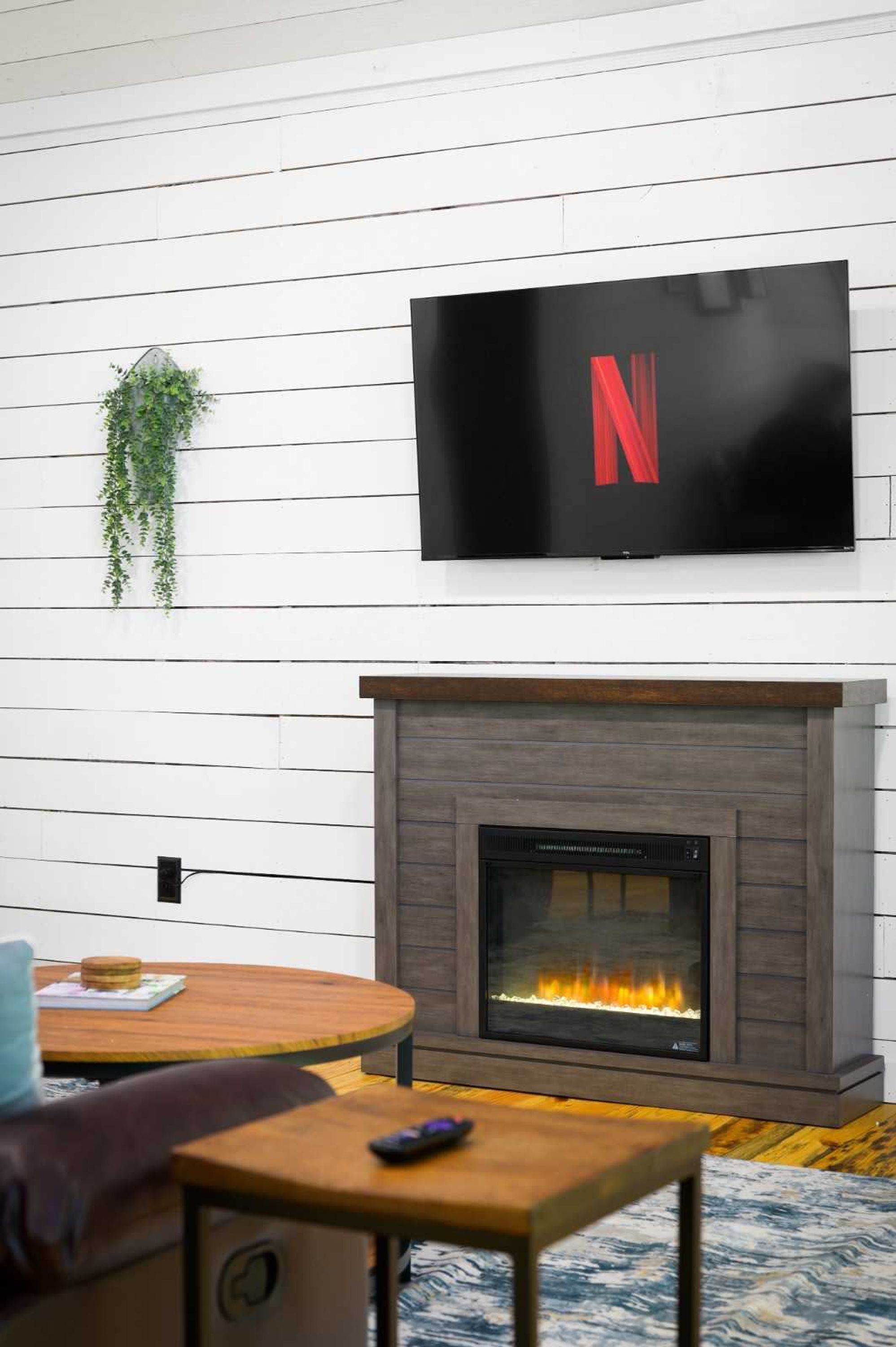 Una sala de estar moderna con chimenea, un televisor montado y una mesita con un control remoto.