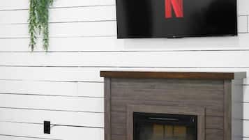 Una sala de estar moderna con chimenea, un televisor montado y una mesita con un control remoto.