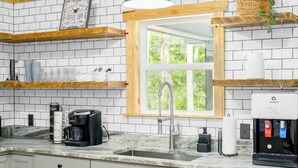 Een keuken met witte metrotegels, houten planken, een koffieapparaat en een waterdispenser.