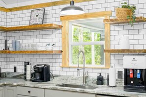 Una cocina con azulejos tipo metro blancos, estantes de madera, una máquina de café y un dispensador de agua.