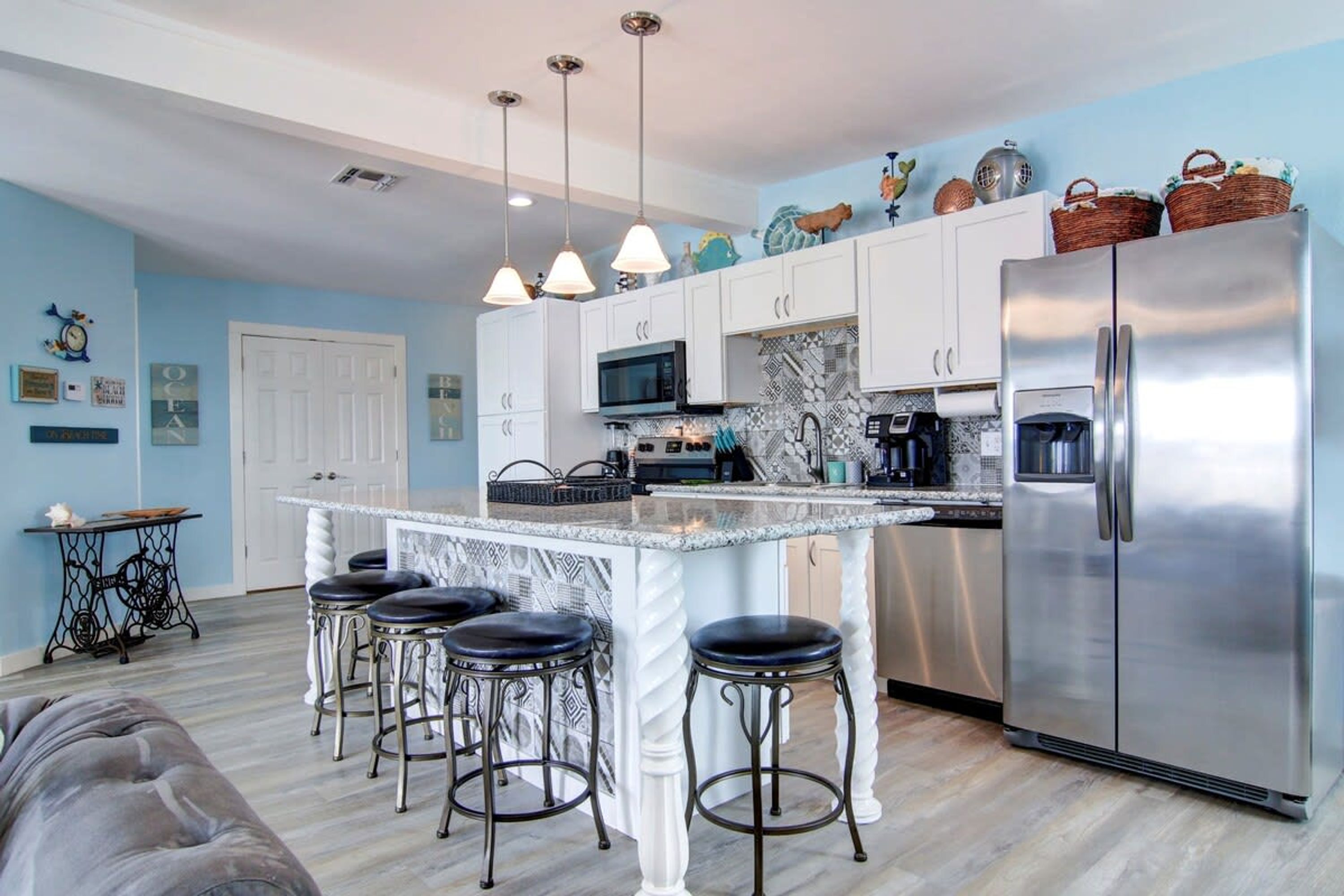 A modern kitchen with a central island, bar stools, a stainless steel refrigerator, and decorative wall art.