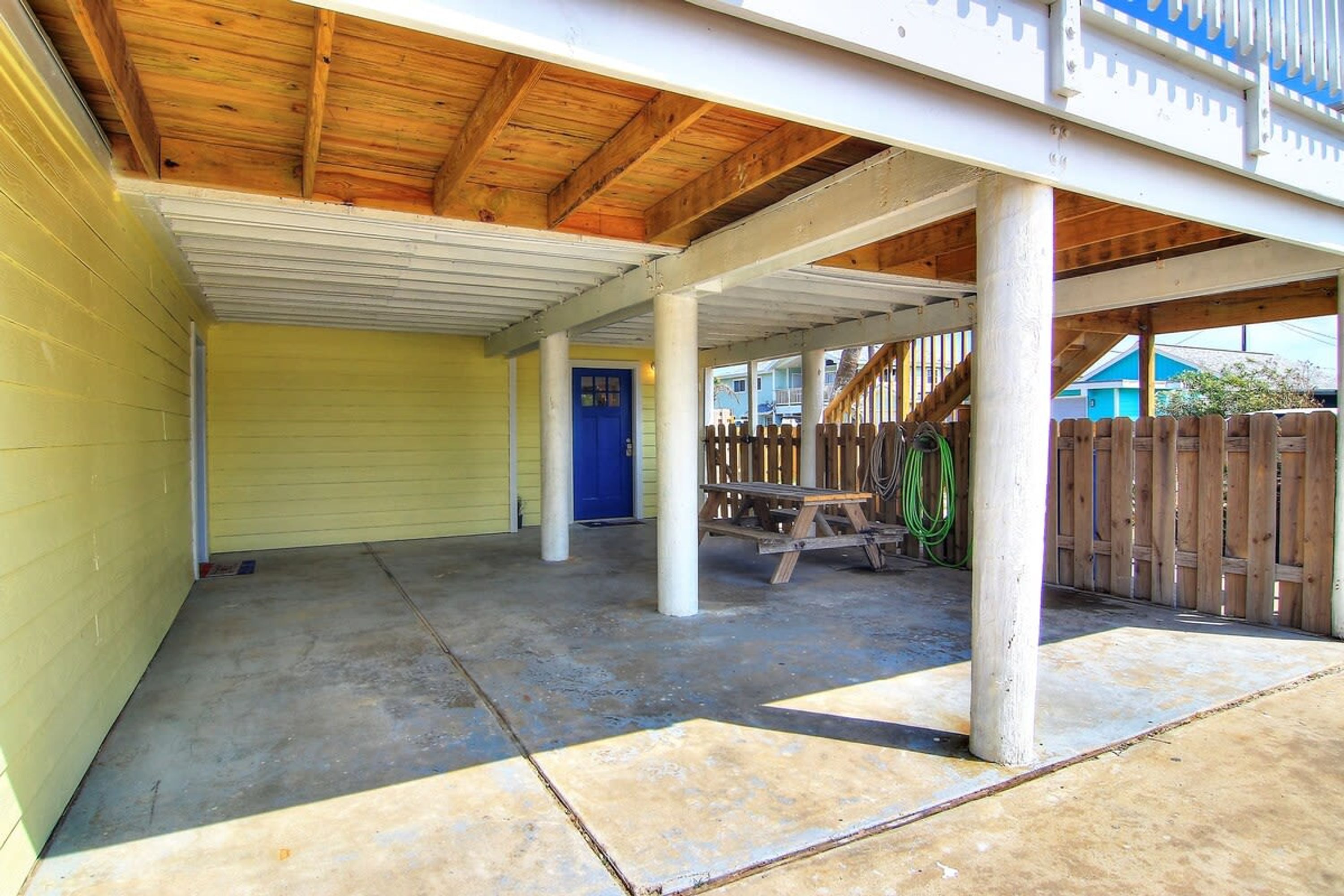 A covered outdoor area with a concrete floor, wooden beams, and a blue door.