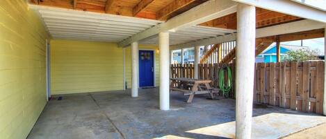 A covered outdoor area with a concrete floor, wooden beams, and a blue door.