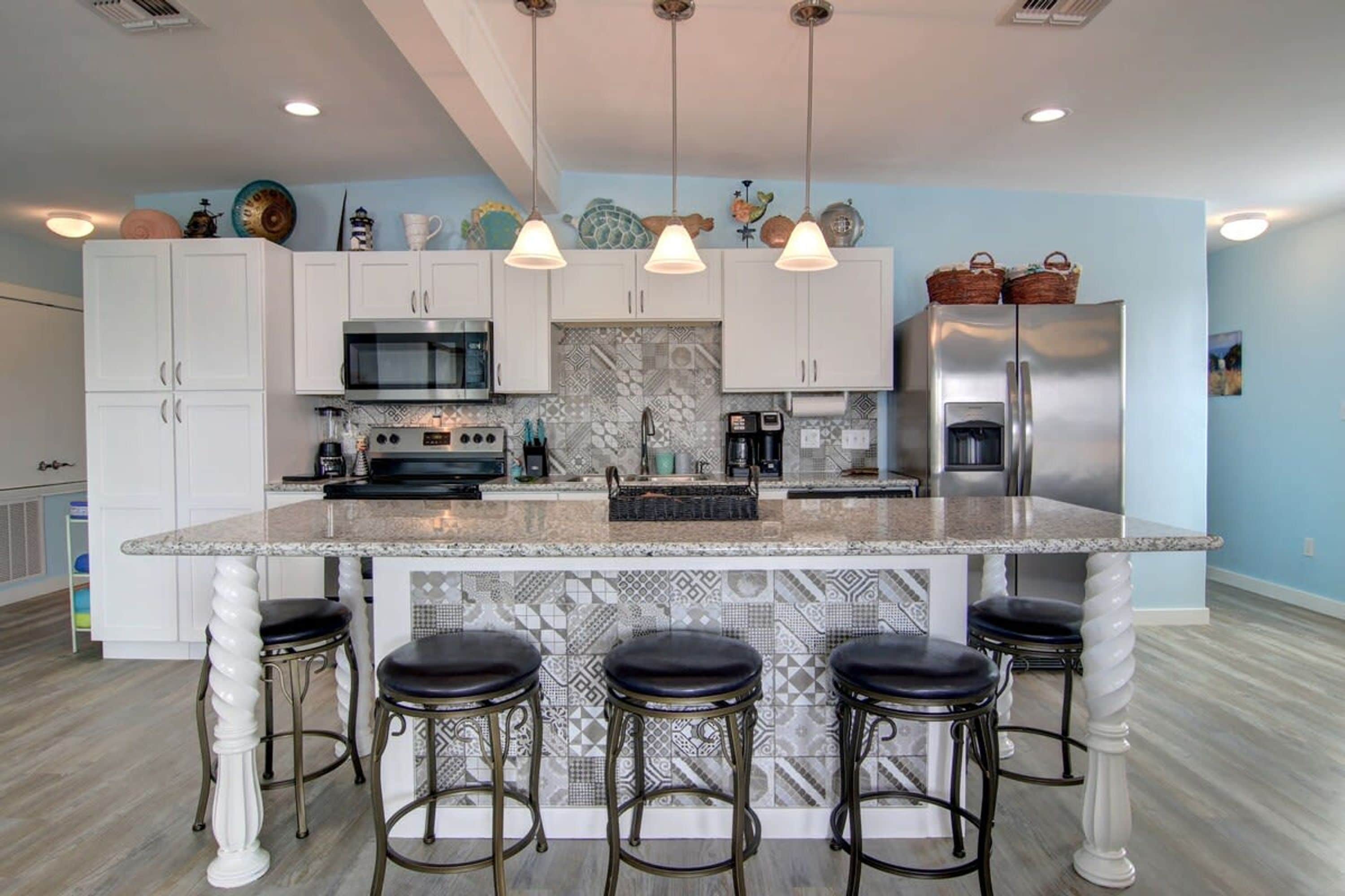 A modern kitchen with white cabinets, a central island with bar stools, stainless steel appliances, and decorative items on the ceiling.