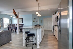 A modern kitchen with a central island, bar stools, pendant lighting, and a refrigerator. - Nauti Mermaid Private Pool Sleeps 14 Dog Friendly (Port Aransas)