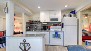 A compact kitchen with white cabinets, a microwave, a stove, and a refrigerator. There is a small island with a sign that reads '13 00'. - Nauti Mermaid Private Pool Sleeps 14 Dog Friendly (Port Aransas)